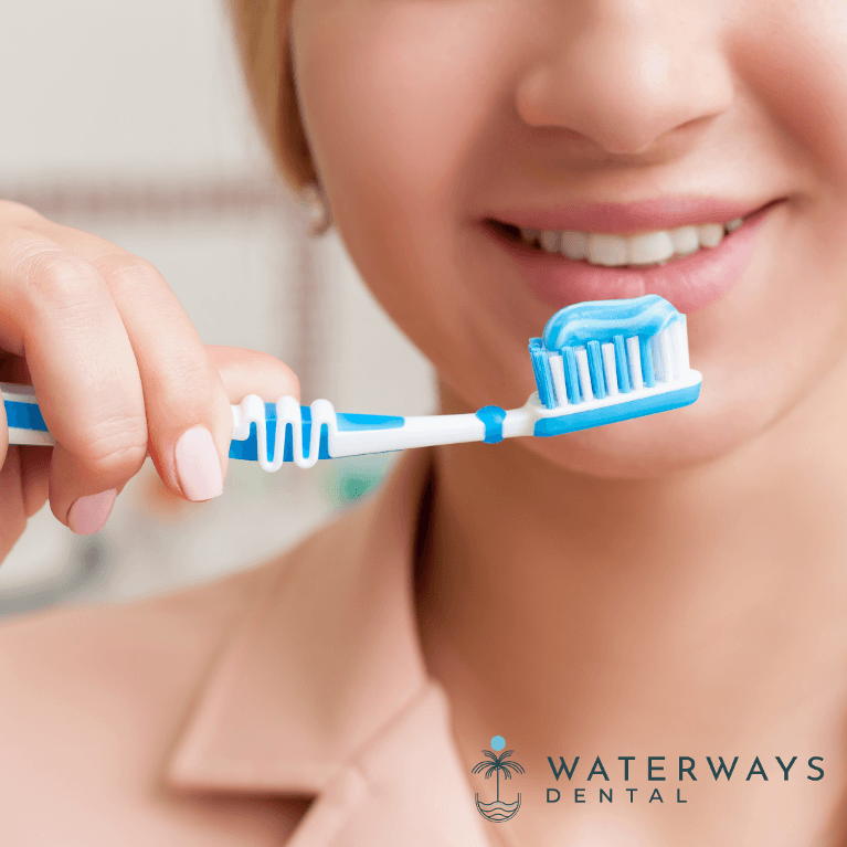 Smiling woman holding a blue toothbrush with blue and white toothpaste applied